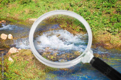 Control of purity and quality of water in nature - concept image with water of a stream seen through a magnifying glass