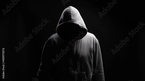Fun psychopath with toys. Silhouette of a man with a darkened face in a hood on a black background. A portrait of a murderer, a hacker. photo
