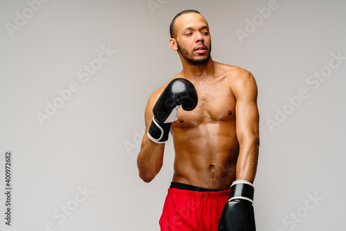 Confident young African boxer in boxing gloves standing over light grey background © Anatoly Repin