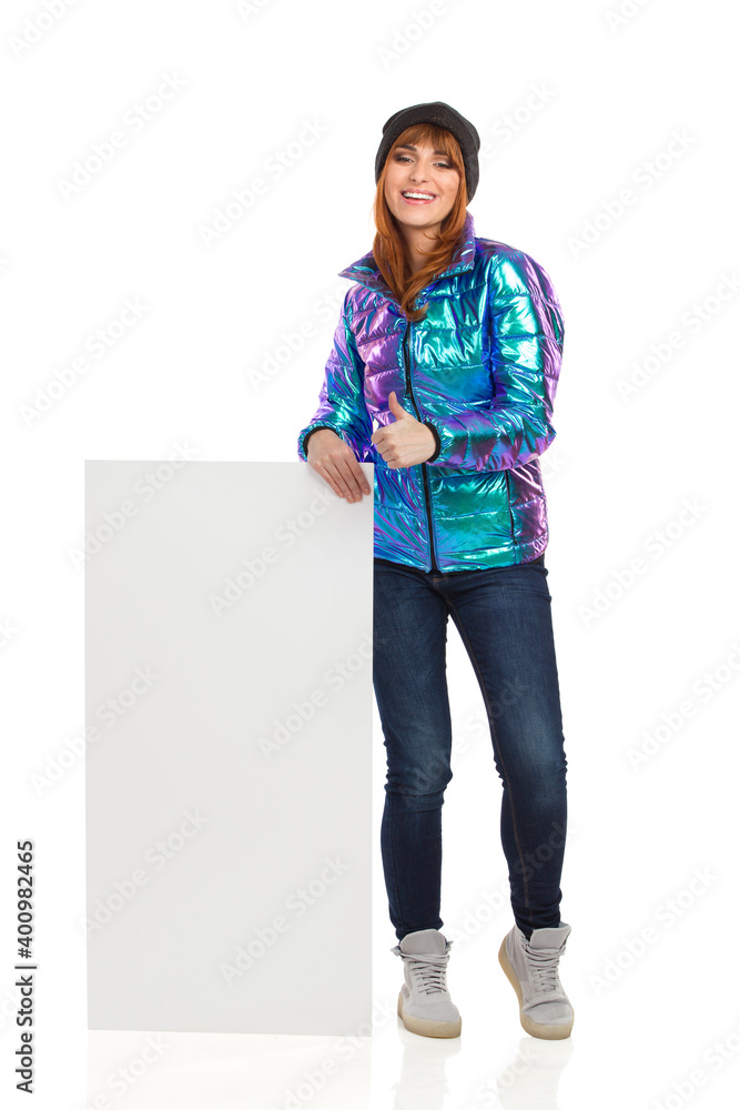 Fototapeta premium Happy Young Woman In Winter Clothes Is Posing With White Banner And Showing Thumb Up