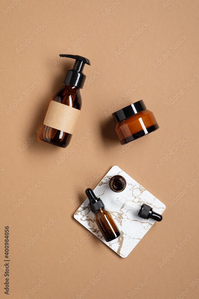 Set of organic cosmetics on brown background. Amber glass bottle with lotion, jar of natural cream, dropper bottle of essential oil. Flat lay, top view.