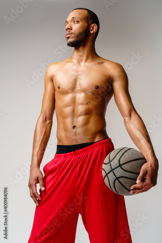 Muscular african american sportsman playing basketball shitless over light grey background photo