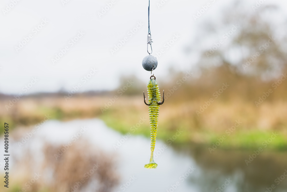 Khakki silicone lure for fishing. Silicone bait for fishing hanging on a hook on the background of the river Khakki silicone lure for fishing. Silicone bait for fishing hanging on a hook on the background of the river
