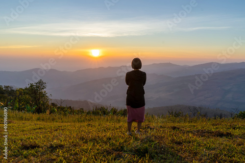 Young woman traveler looking at the sunrise over the mountain