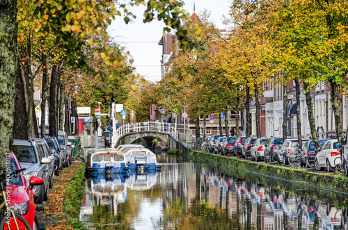 Delft, The Netherlands, November 11, 2020: tourist boats, parked cars and trees in autumn colors at Koornmarkt canal in the old town