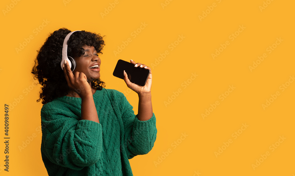 Black woman with smartphone and headset singing on yellow Black woman with smartphone and headset singing on yellow