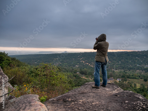 a traveler standing on top of high cliff and taking some picture.