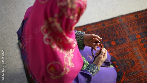 Closeup of a muslim woman hands while praying with prayer beads on prayer rug.