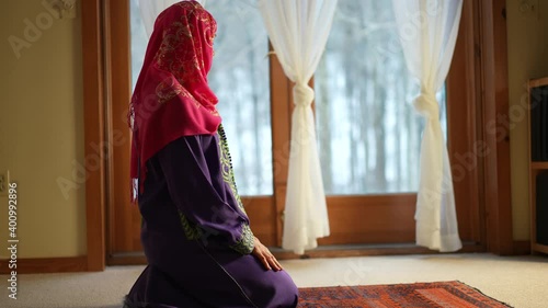 Mature Muslim woman praying at home with beautiful light with snow on the ground. Concept of female prayer in home environment.