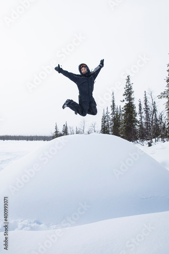 Girl jumping for joy on a snow mountain in overalls and hat