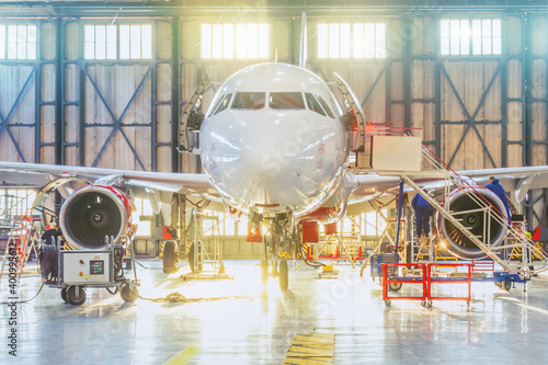 Aircraft inside the aviation hangar, maintenance service. Airplane mechanic working around. Bright light of different colors outside the gate.