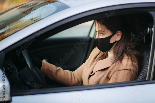 Beautiful young girl in a mask sitting in a car and put on protective gloves. Protective mask against covid-19, driver on a city street during a coronavirus outbreak © Aleksandr