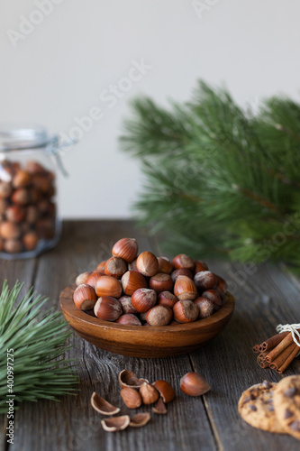 A handful of fresh organic hazelnuts in a wooden bowl on a wooden table among the fir branches. Jar with nuts in the background. Vertical orientation  space for text.