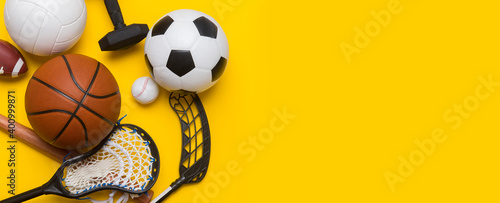 Assorted sports equipment including a soccer ball, volleyball, baseball, american football, lacrosse and hockey on a blue background. Top view, space for your text