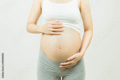 pregnant woman caressing her belly over gray background-Motherhood, pregnancy, people and expectation concept. © Ann Patchanan