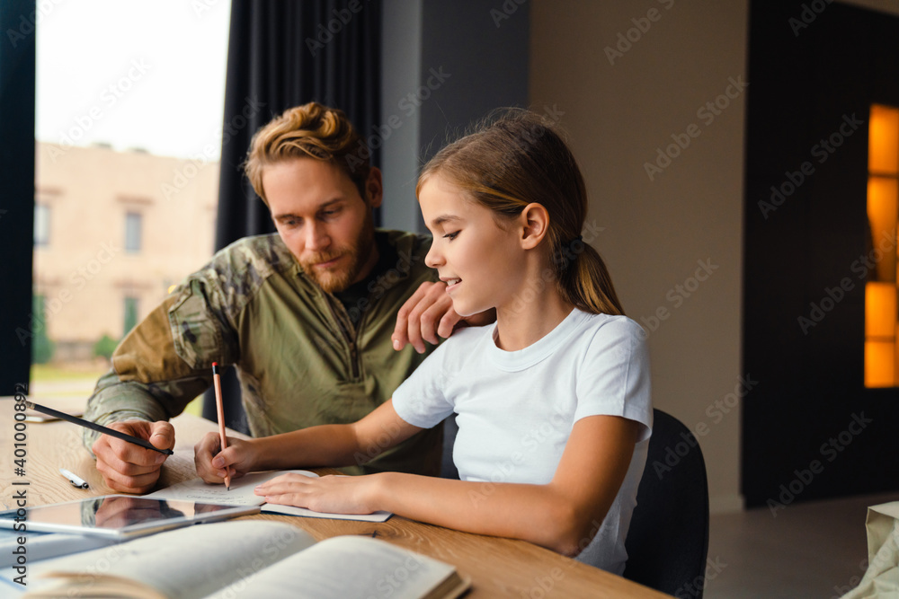 Masculine focused military man doing homework with her daughter at home Masculine focused military man doing homework with her daughter at home