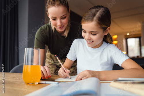 Beautiful happy military woman doing homework with her daughter at home