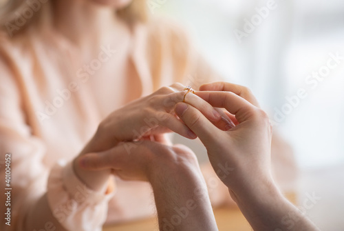 Closeup of young man putting diamond engagement ring on his girlfriend s finger  making marriage proposal at cafe