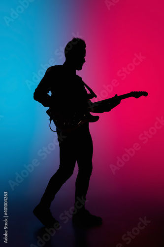 Party. Silhouette of young male guitarist isolated on blue-pink gradient studio background in neon. Beautiful shadow in action, performing. Concept of human emotions, expression, ad, music, art.
