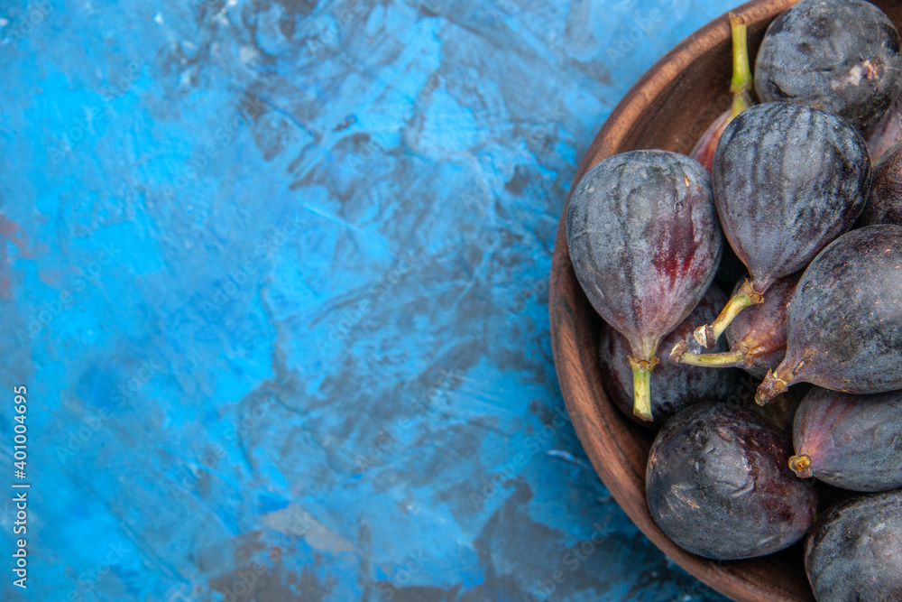 Half shot of black mission figs in a small brown pot on the right side on blue background