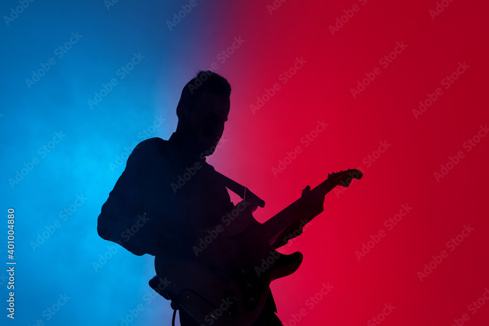 Smoke. Silhouette of young male guitarist isolated on blue-pink gradient studio background in neon. Beautiful shadow in action, performing. Concept of human emotions, expression, ad, music, art.