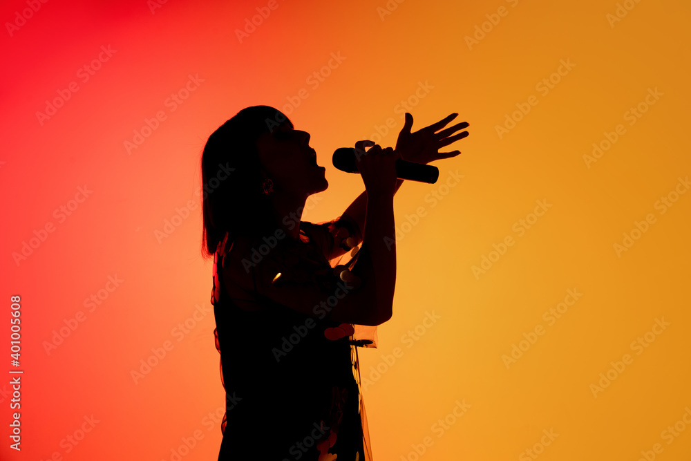 Inspired. Silhouette of young female singer isolated on orange gradient studio background in neon light. Beautiful shadow in action, performing. Concept of human emotions, expression, ad, music, art.