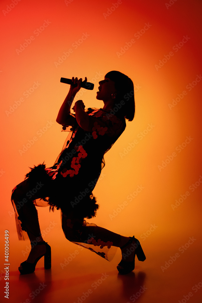 Party. Silhouette of young female singer isolated on orange gradient studio background in neon light. Beautiful shadow in action, performing. Concept of human emotions, expression, ad, music, art.