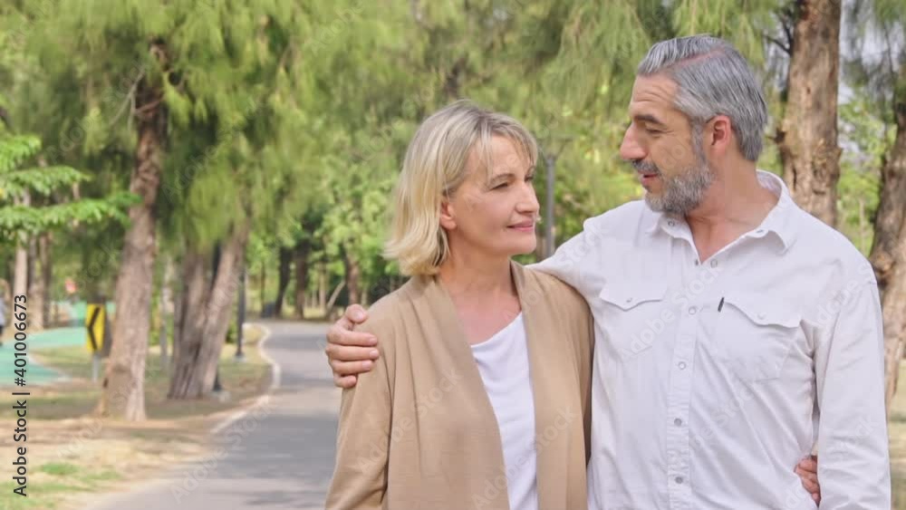 senior couple walking and talking together in the park. after retirement lifestyle. husband embrace wife's shoulder with love. concept for family or insurance senior couple walking and talking together in the park. after retirement lifestyle. husband embrace wife's shoulder with love. concept for family or insurance