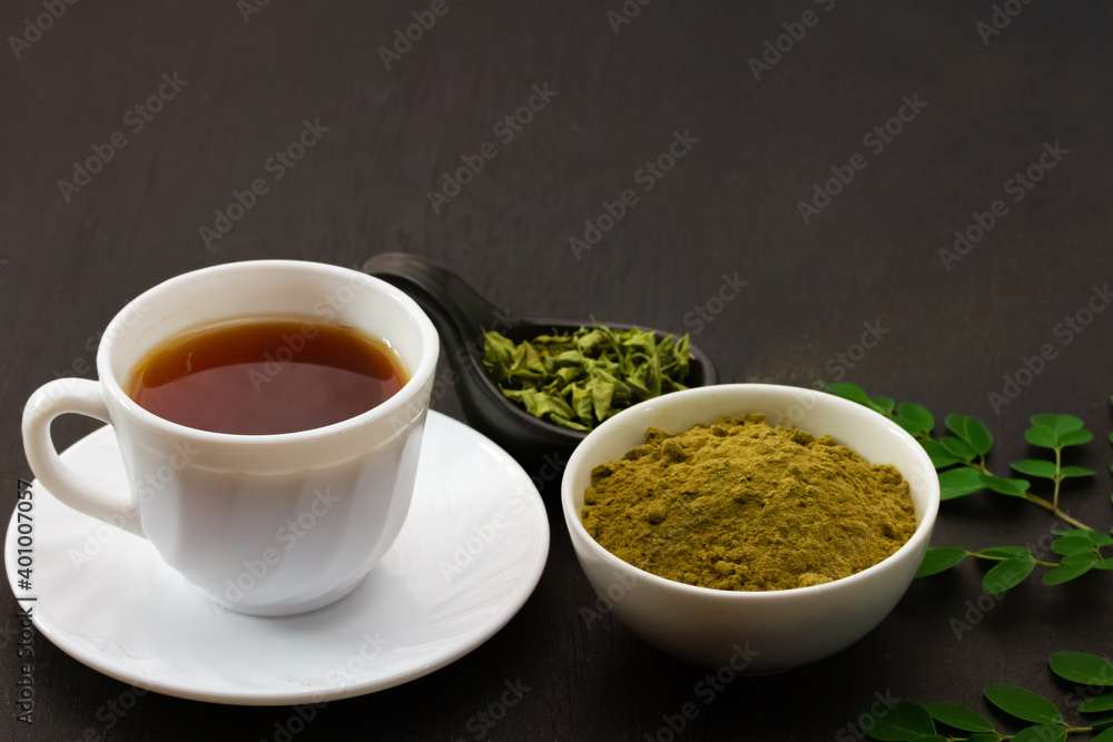 moringa tea in white cup ceramic and moringa leaf on black wooden background moringa tea in white cup ceramic and moringa leaf on black wooden background