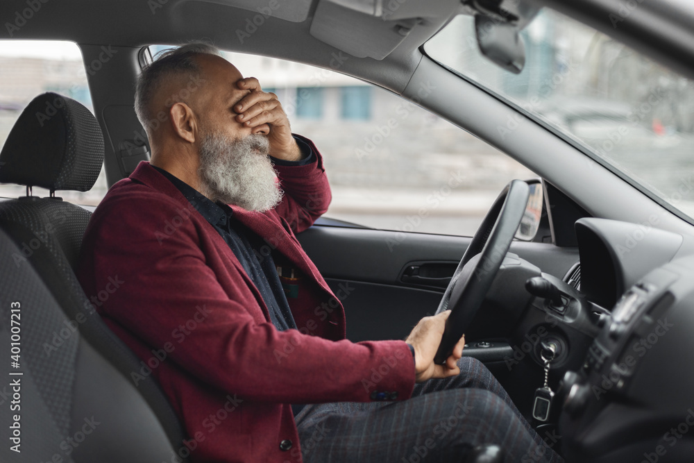 Exhausetd aged grey-haired man having headache while driving car Exhausetd aged grey-haired man having headache while driving car