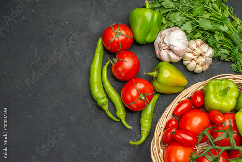 Horizontal view of fresh various organic vegetables inside and outside of a wicker basket on the left side on dark background