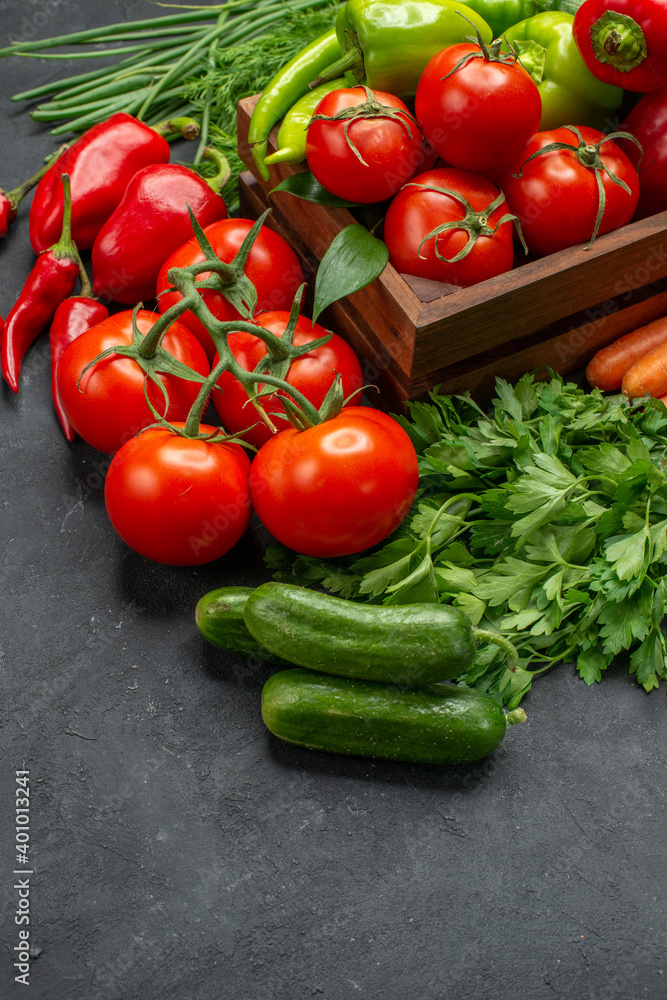 Front close view of vegetable basket with a bunch of green and peppers cucumber and tomatoes with stem carrots beets on dark background Front close view of vegetable basket with a bunch of green and peppers cucumber and tomatoes with stem carrots beets on dark background