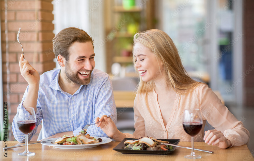 Happy young couple having lunch together at cafe, talking and laughing during meal