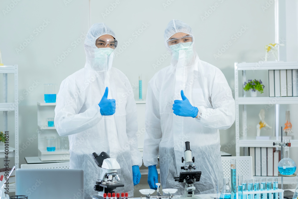 Two scientists wearing personal protective and safety glass standing and thumb up in the laboratory. Research on the coronavirus vaccine to prevent COVID-19. Medical and health concept. Two scientists wearing personal protective and safety glass standing and thumb up in the laboratory. Research on the coronavirus vaccine to prevent COVID-19. Medical and health concept.