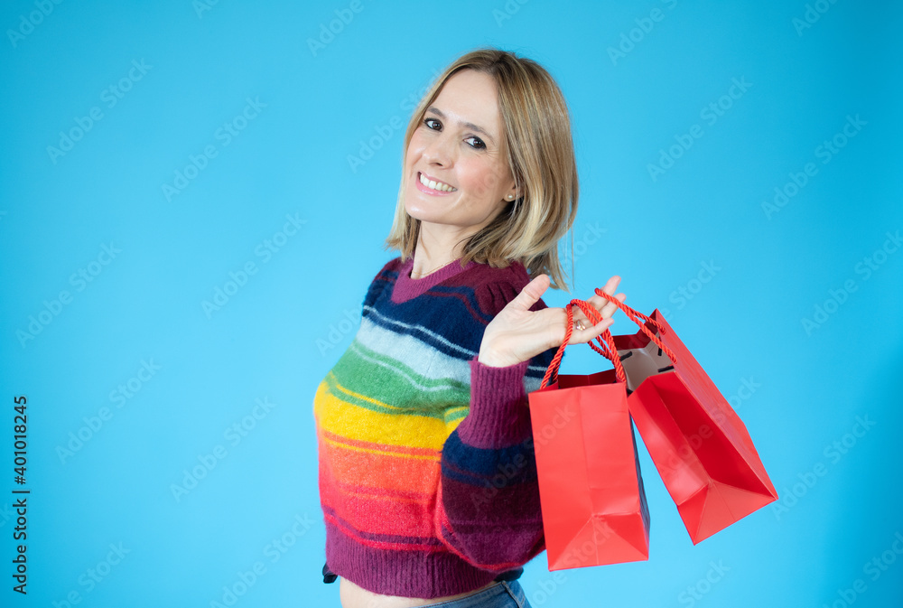 Image of happy young woman standing isolated over blue background holding shopping bags. Looking camera. Image of happy young woman standing isolated over blue background holding shopping bags. Looking camera.