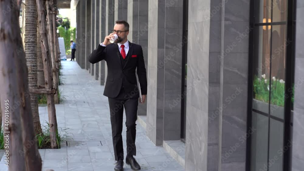 Business man in suit holding laptop computer walking and drinking coffee of disposable paper cup take a away outside office Business man in suit holding laptop computer walking and drinking coffee of disposable paper cup take a away outside office
