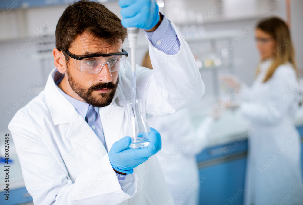 Young researcher in protective workwear standing in the laboratory and analyzing flask with liquid Young researcher in protective workwear standing in the laboratory and analyzing flask with liquid