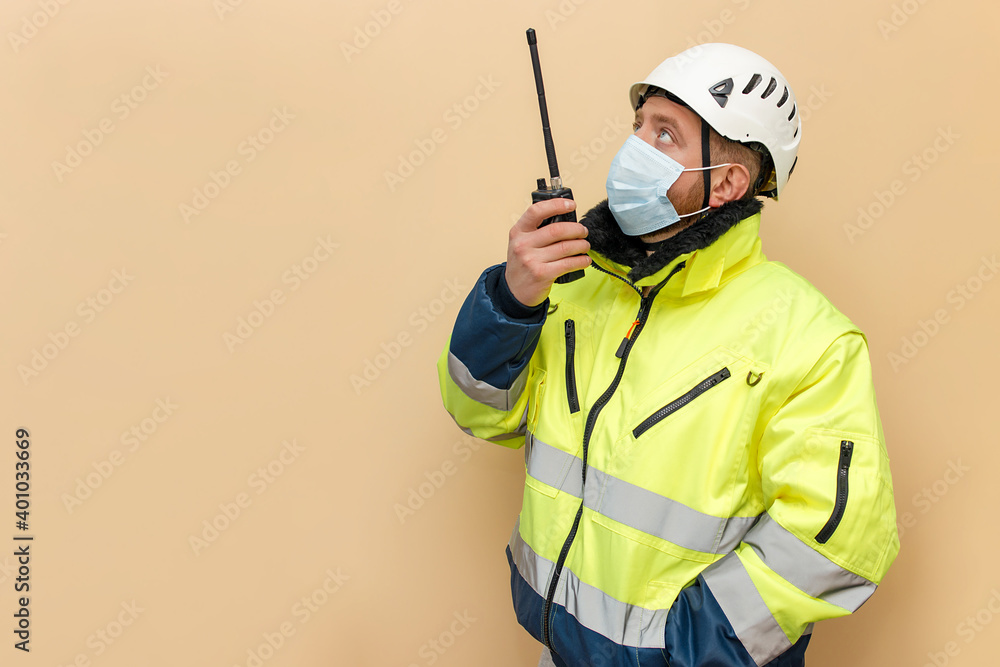 Male bearded industrial worker in hard hat with walkie-talkie. Man engineer with white hard hat. Worker with medical mask. Climber Male bearded industrial worker in hard hat with walkie-talkie. Man engineer with white hard hat. Worker with medical mask. Climber