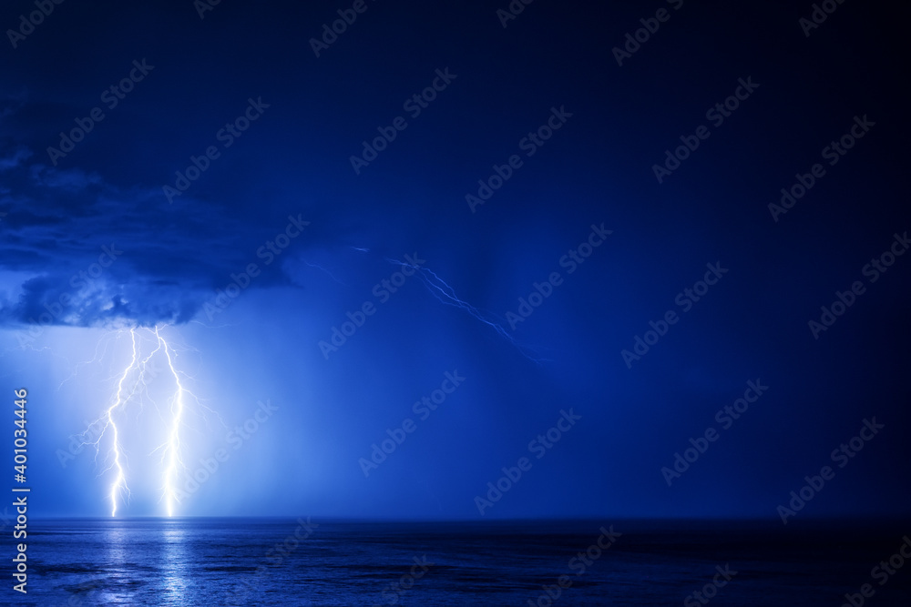 Two lightning bolts over the sea with a reflection in the left part of the frame on a dark blue cloud background