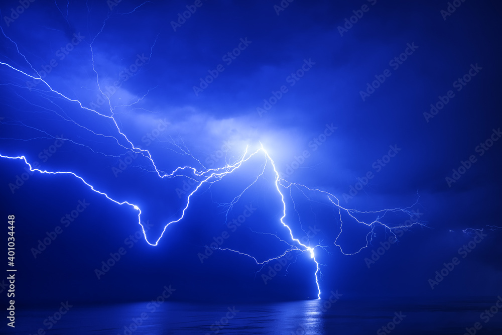 A huge branched lightning strikes the sea near a distant ship with a reflection