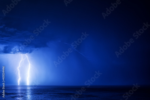 Two lightning bolts over the sea with a reflection in the left part of the frame on a dark blue cloud background