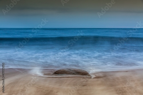 A single rock on the beach as the wave backwash returns to the sea over the sand on a cloudy day  2 