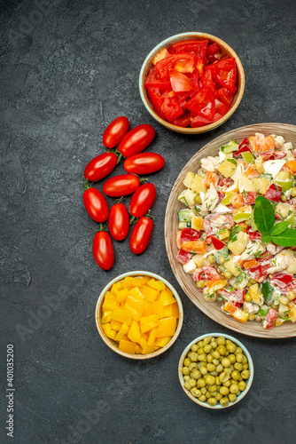 top view of bowl of vegetable salad with vegetables on side on dark grey background