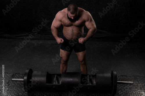 an athlete with voluminous muscles stands next to an apparatus for power extreme.
