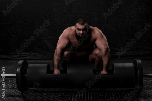 the bearded strongman crouched down and prepares to lift a large metal log