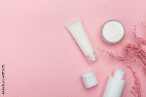 Cosmetic products and branch of flowers on pastel pink background. Concept natural cosmetics, beauty, skincare. Top view, flat lay, copy space