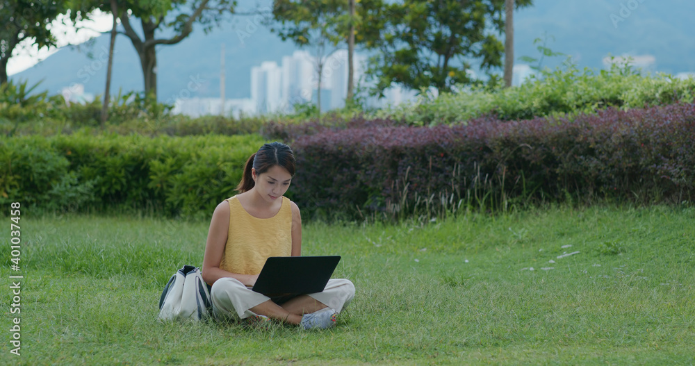 Woman work on laptop computer and sit on green lawn