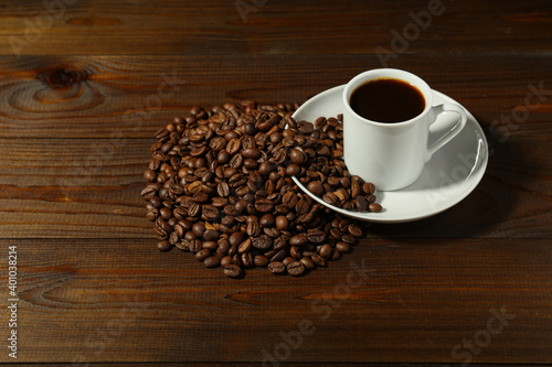 white coffee cup and coffee beans are on a wooden background. 