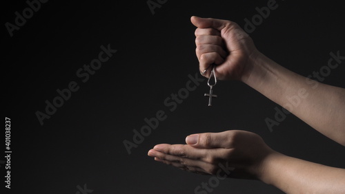 Cross or crucifix pendant and necklace in man hand on black color background in studio which represent praying for god or jesus and thank gods for giving peaceful and faithful to people. silver cross.
