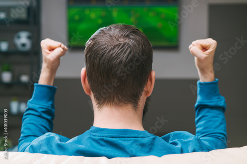 Man spending day-off at home, sitting on sofa, watching football play on tv cheering for favourite team